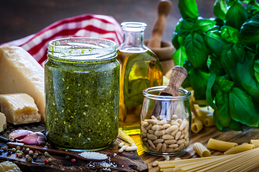 Front view of an open glass jar filled with original Genovese pesto sauce. Ingredients for pesto sauce preparation are olive oil, basil leaves, garlic, pine nut, Parmesan cheese, salt and pepper. Low key DSRL studio photo taken with Canon EOS 5D Mk II and Canon EF 100mm f/2.8L Macro IS USM