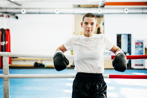 A portrait of a female kickboxer leaning on the ropes at her local gym.