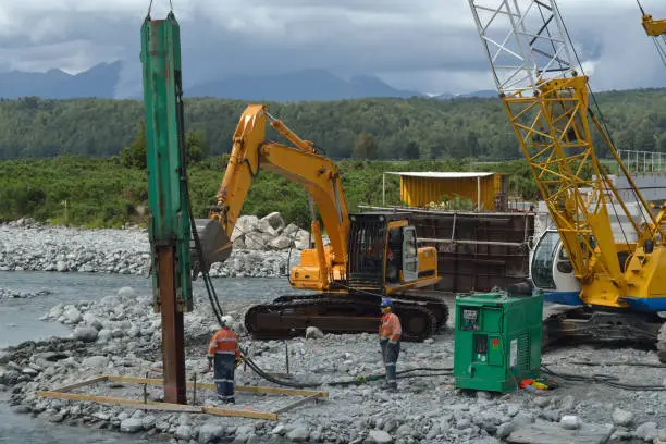Builders drive pylons for a concrete bridge over a river in Westland, New Zealand