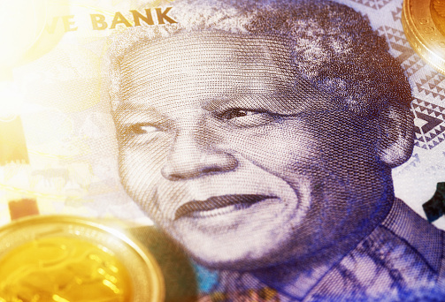 Face of Nelson Mandela on a large-denomination South African banknote wth Five Rand coin alongside.
