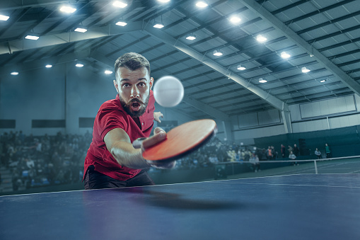 The table tennis player in motion. Fit young sports man tennis-player in play on sport arena background with lights. Movement, sport game, stobe concepts. Professional. Human emotions, facial expression. 3D model of the stadium was created by me (the author)