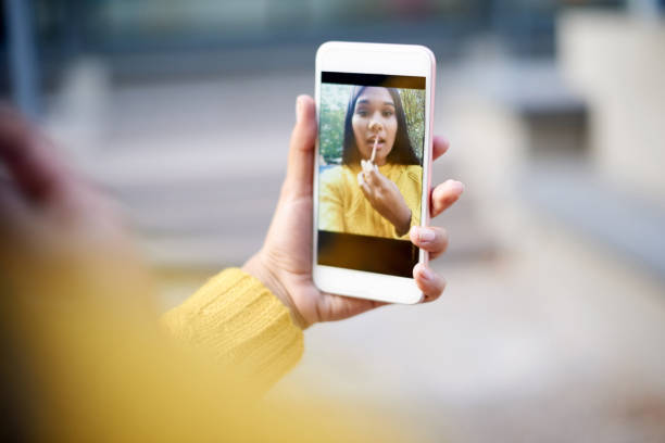 Cropped shot of a beautiful young woman applying make up using her front camera on her cellphone as a mirror outside