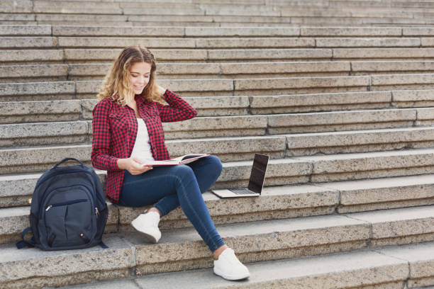istock Smiling female student sitting on the stairs using laptop outdoo 970175498