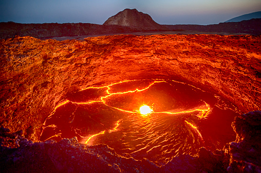 View from the crater rim of Erta Ale - one of the most active vulancoes in the world - into the active, red glowing lava lake. Erta Ale is a continuously active basaltic shield volcano in the Afar Region of northeastern Ethiopia, only some kilometers from the border to Eritrea.\n\nThe Afar Depression (or Danakil Depression) in the border-triangle between Ethiopia, Eritrea and Djibouti is one of the most remote and most extreme regions of the world - it is the lowest point in Africa (- 155 metres/-550 ft below sea level) and one of the hottest places on Earth.\n\nThe Danakil/Afar Depression is the product of a tectonic triple junction, where the spreading ridges that form the Red Sea and the Gulf of Aden emerge on land and meet the East African Rift. Here the Earth's crust is slowly rifting apart at a rate of 1–2 centimetres (0.3–0.8 in) per year.\n\nErta ale is ond of the most dangerous places on earth - the lat major eruptions took place in September 2005, August 2007 and November 2008.