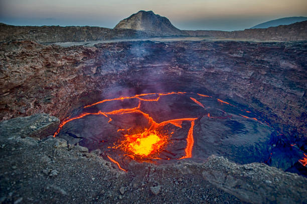 View into the lava lake of Erta Ale volcano, Ethiopia View from the crater rim of Erta Ale - one of the most active vulancoes in the world - into the active, red glowing lava lake. Erta Ale is a continuously active basaltic shield volcano in the Afar Region of northeastern Ethiopia, only some kilometers from the border to Eritrea.

The Afar Depression (or Danakil Depression) in the border-triangle between Ethiopia, Eritrea and Djibouti is one of the most remote and most extreme regions of the world - it is the lowest point in Africa (- 155 metres/-550 ft below sea level) and one of the hottest places on Earth.

The Danakil/Afar Depression is the product of a tectonic triple junction, where the spreading ridges that form the Red Sea and the Gulf of Aden emerge on land and meet the East African Rift. Here the Earth's crust is slowly rifting apart at a rate of 1–2 centimetres (0.3–0.8 in) per year.

Erta ale is ond of the most dangerous places on earth - the lat major eruptions took place in September 2005, August 2007 and November 2008. danakil desert photos stock pictures, royalty-free photos & images