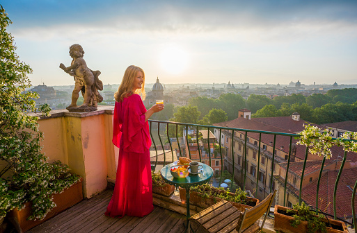 Female standing on romantic balcony with glass of fresh orange juice