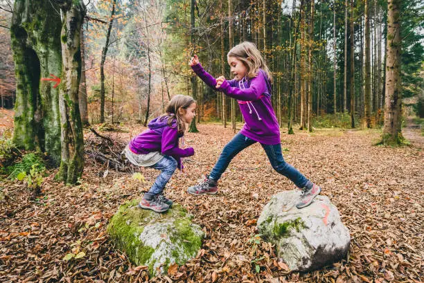 Photo of Identical twins are jumping from rocks in forest on hiking.