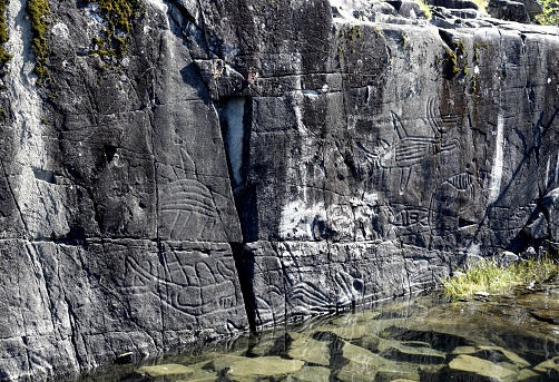 closeup of lake shore rock showing petroglyphs of prehistorical  mystical figures, Sproat Lake BC Canada