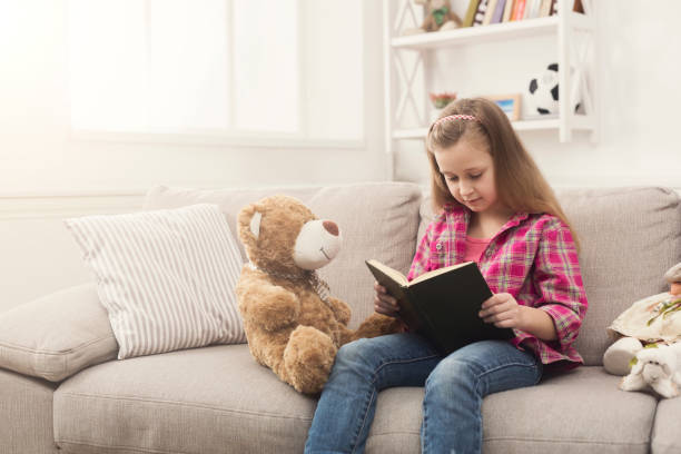istock Happy little child reading book for her teddy bear 970218218