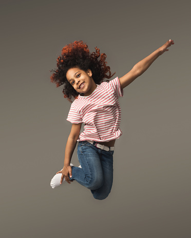 Beautiful little african-american girl jumping a gray studio background, copy space. Studio shot of cute happy child