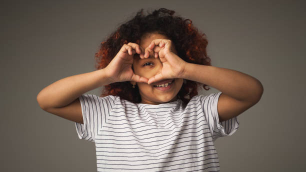 menina feliz preta com os dedos em forma de coração, retrato de estúdio - dark little girls child happiness - fotografias e filmes do acervo