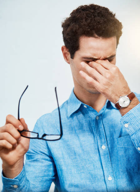 müder junger mann reibt sich die augen, als er seine brille hält - human eye rubbing tired glasses stock-fotos und bilder