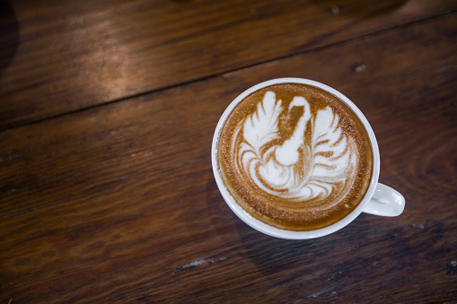top view of Coffee cup with bird latte art on wooden table . Selective focus white cup.color vintage style.