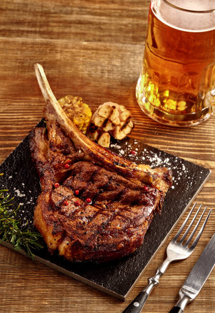 grillé, steak de boeuf de cowboy, verre de bière, des herbes et des épices sur un fond en bois. vue de dessus - steak argentina food silverware photos et images de collection