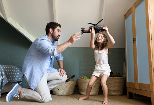 Playful father and daughter with toy helicopter. Man is playing with girl at home. They are wearing casuals.