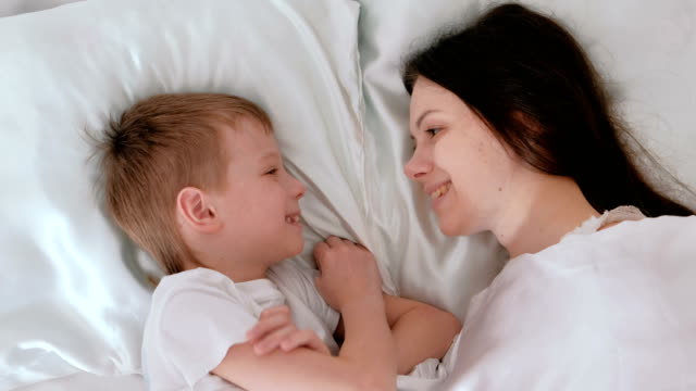 Mom and son wake up. Mom kisses and hugs her son.