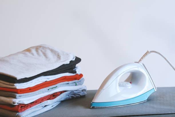 istock Close up view of iron clothes on ironing board with stack of ironed shirts 970271396