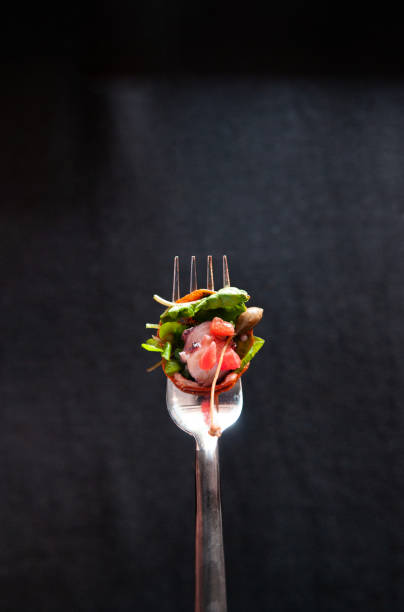 istock Octopus carpacio with citrus spinach salad pesto balsamic dressing on silver fork, isolated on dark background 970281430