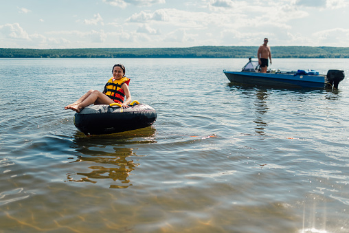 the girl on the inflatable pillow is smiling, preparing to skate after the boat on the lake.