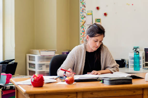 Teacher working at her desk in empty classroom. stock photo