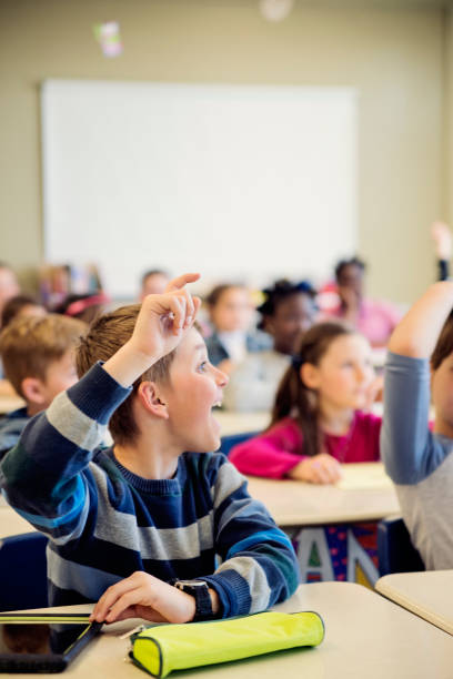 istock Elementary school children with arms raised in classroom. 970309470