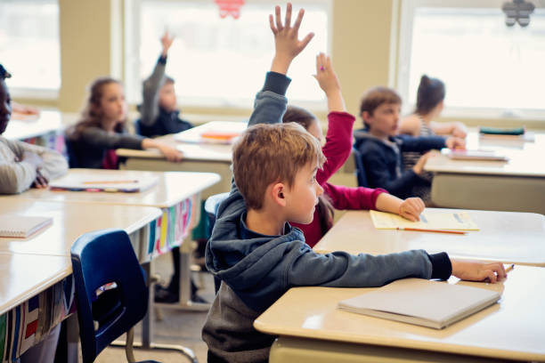 istock Elementary school children with arms raised in classroom. 970309638