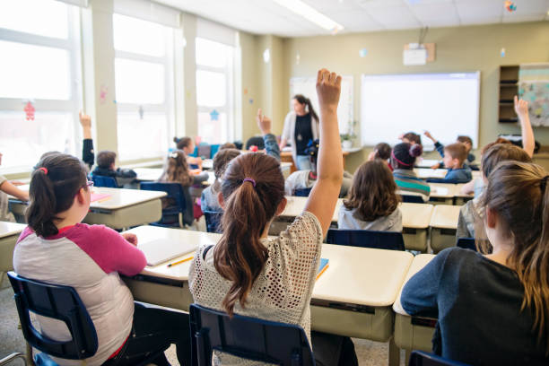 Elementary school children with arms raised in classroom. stock photo