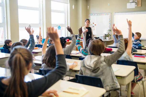 istock Elementary school children with arms raised in classroom. 970310088