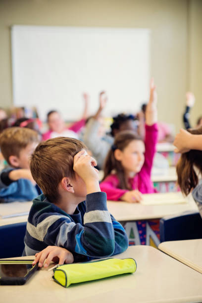 istock Elementary school children with arms raised in classroom. 970310436