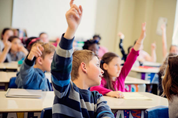 istock Elementary school children with arms raised in classroom. 970310494