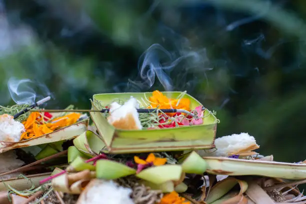 Photo of Burning incense sticks surrounded with Balinese offerings outside on a hindu temple in Ubud, Bali, Indonesia.