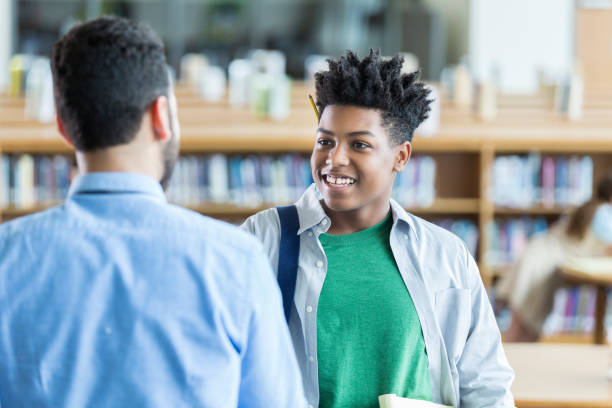 istock Teenage boy greets teacher in school library 970320182
