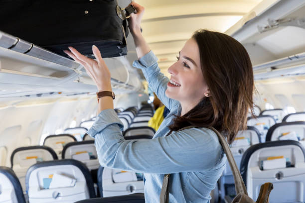 mujer joven pone llevar en bolsa en el compartimiento arriba del avión - equipaje de mano fotografías e imágenes de stock