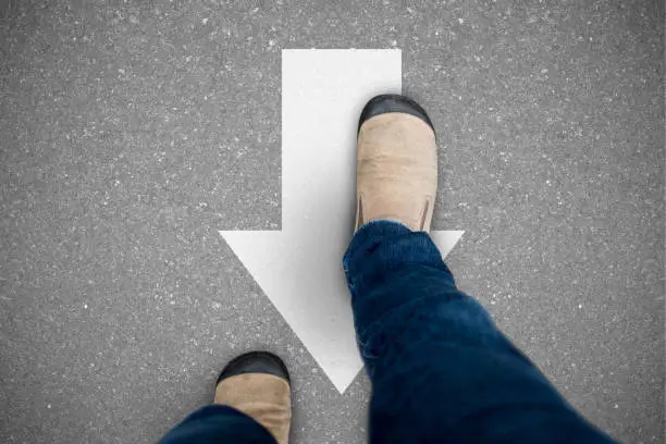 One wearing jeans and brown suede shoes walking on opposite direction path representing think different, new idea, liberal, contrary, unique.