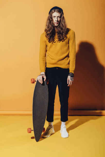 istock young stylish skater standing with longboard, on yellow 970361982