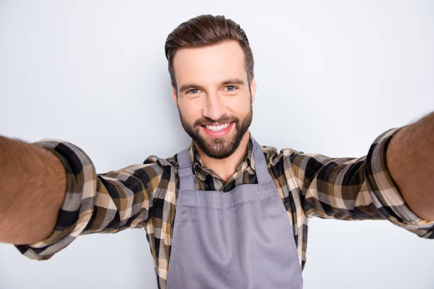 retrato del uno mismo de moda elegantes panadero con peinado tiro selfie en teléfono inteligente con las dos manos, aislado en fondo gris, tener video llamada durante pausa pausa tiempo de espera - commercial kitchen bakery front view baking fotografías e imágenes de stock