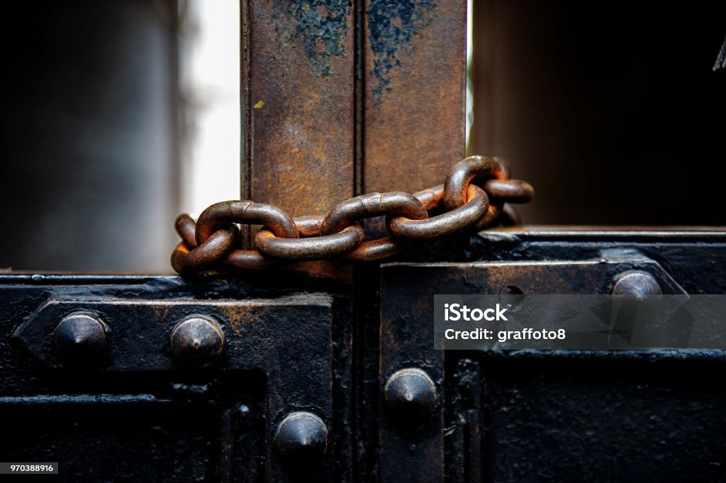 old metal gates are covered with a rusty metal chain. old metal gates are covered with a rusty metal chain. In an urban environment. Closed Stock Photo
