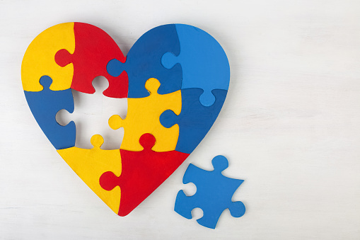 A colorful heart made of symbolic autism puzzle pieces on white wooden background