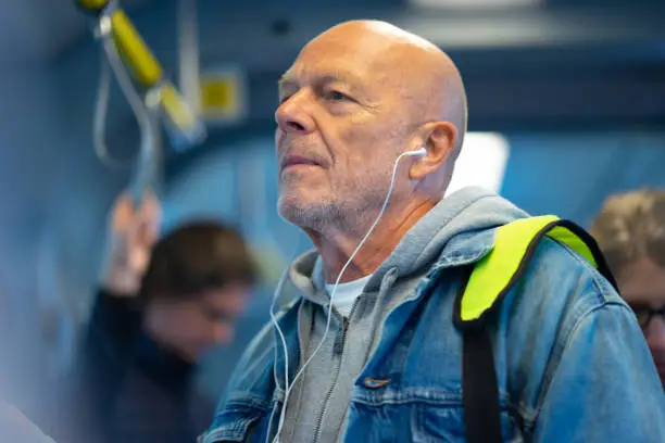 Photo of Senior man listening to earphones on public transport