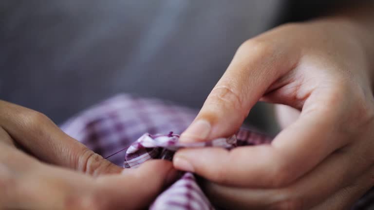 woman with needle stitching on button to shirt