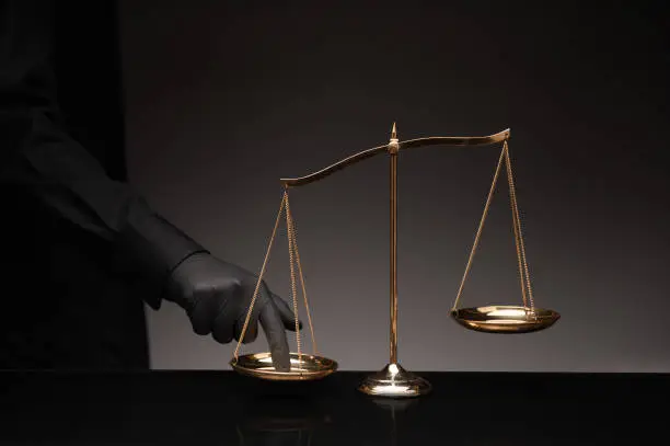 Man wearing black shirt pressing the imbalance scale on black glass desktop and black background, cheating  in a lawyer's office, Concept of injustice, espionage, partiality, law.