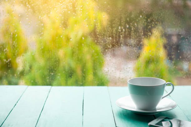 White coffee cup with mobile phone on old green wooden floor White coffee cup with mobile phone on old green wooden floor with raining background in the garden and natural scenery. rainy cafe stock pictures, royalty-free photos & images