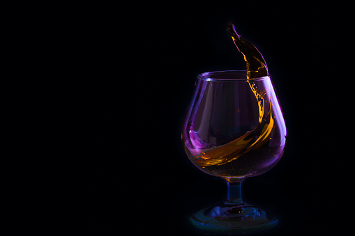 splash in a glass of brandy in colored lighting on a black background