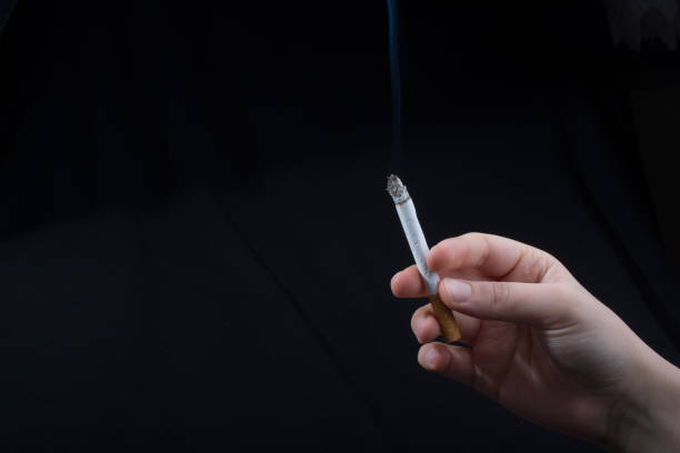 istock Hand is holding smoking cigarette on black background 970425472