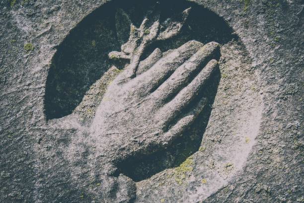 Clasped hands on weathered cemetery gravestone signifying peace and friendship