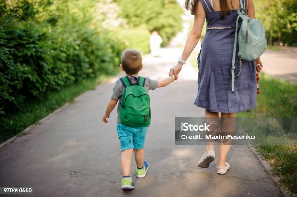 Foto de Vista Traseira Da Mãe Andando Pela Rua Com Um Filho Pequeno Com Uma Mochila Em Dia Ensolarado e mais fotos de stock de Criança