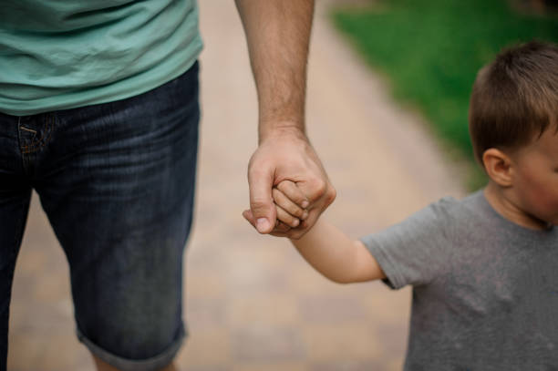 Strong father hand holding a little hand of his son Strong father hand holding a little hand of his son walking down the street on warm day obscured face stock pictures, royalty-free photos & images