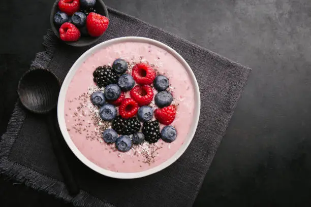 Delicious appetizing smoothie bowl with wild berries on plate on dark background. Top View