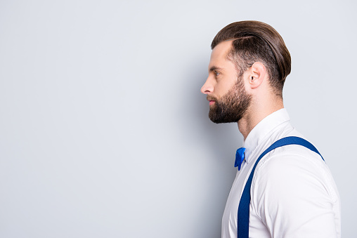 Profile side view portrait with copyspace, empty place for advertisement of famous concentrated singer wearing bow, shirt, suspenders, isolated on grey background