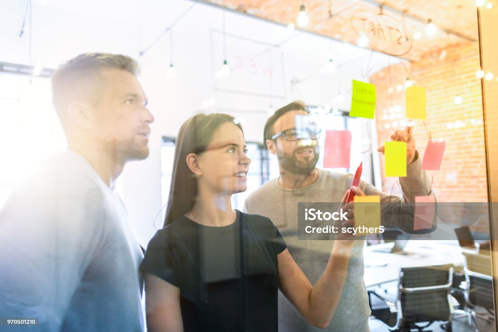 Young creative business people meeting at office. Business people meeting at office and use post it notes to share idea. Brainstorming concept. Sticky note on glass wall. Adhesive Note Stock Photo